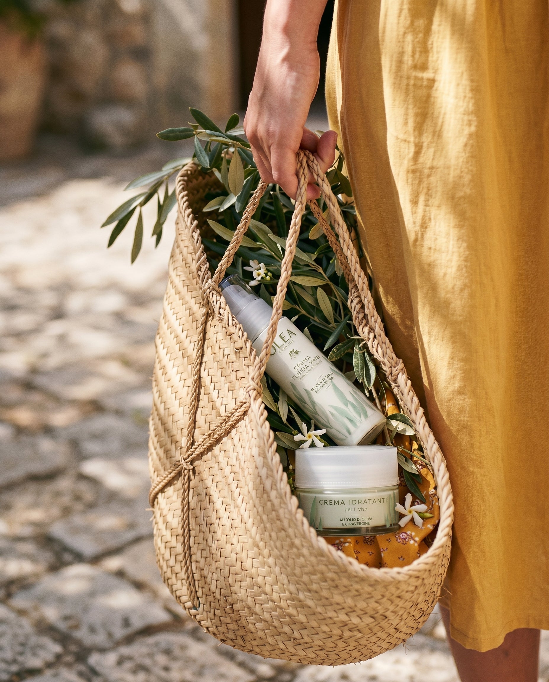Una cesta di vimini con rami d'ulivo, fiori e i prodotti Olea Cosmetics. Oleificio Fratelli Vieste