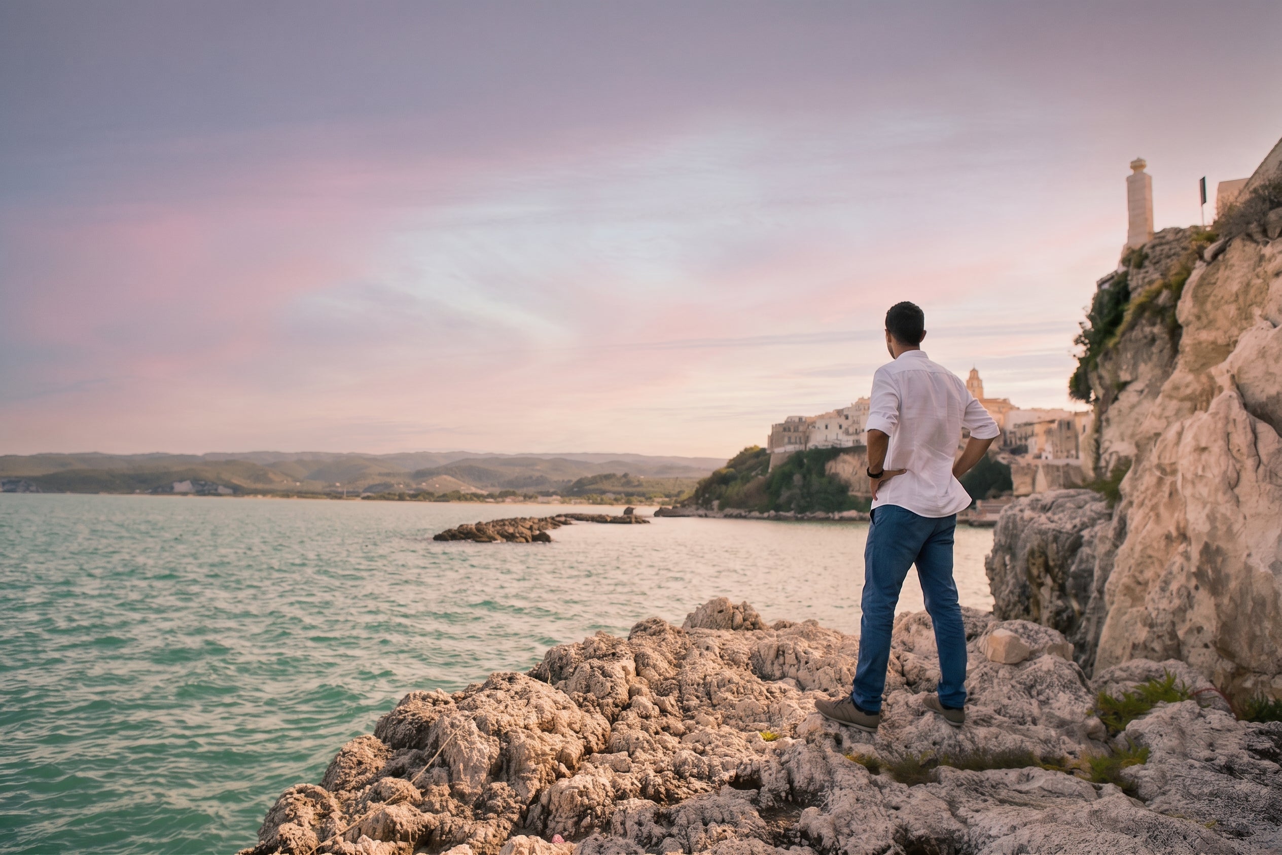 Un uomo osserva dagli scogli il mare e il centro storico di Vieste al tramonto. Oleificio Fratelli Vieste