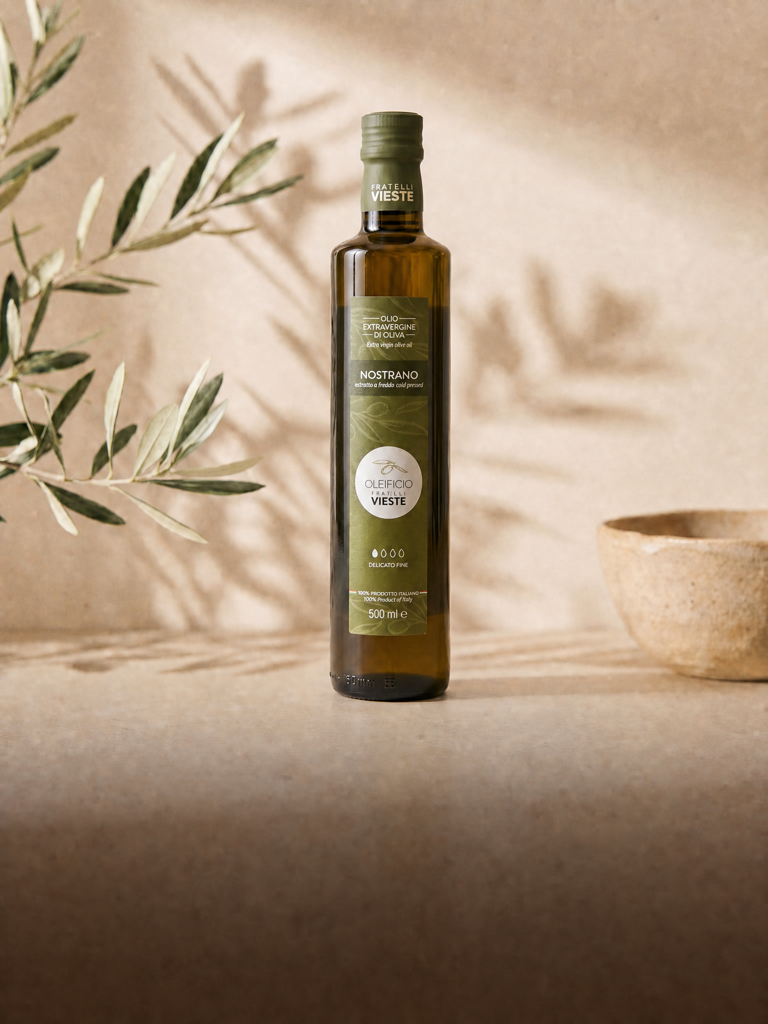 Bottiglia di olio extravergine Nostrano da 500 ml tra le ombre dei rami d'ulivo. Oleificio Fratelli Vieste