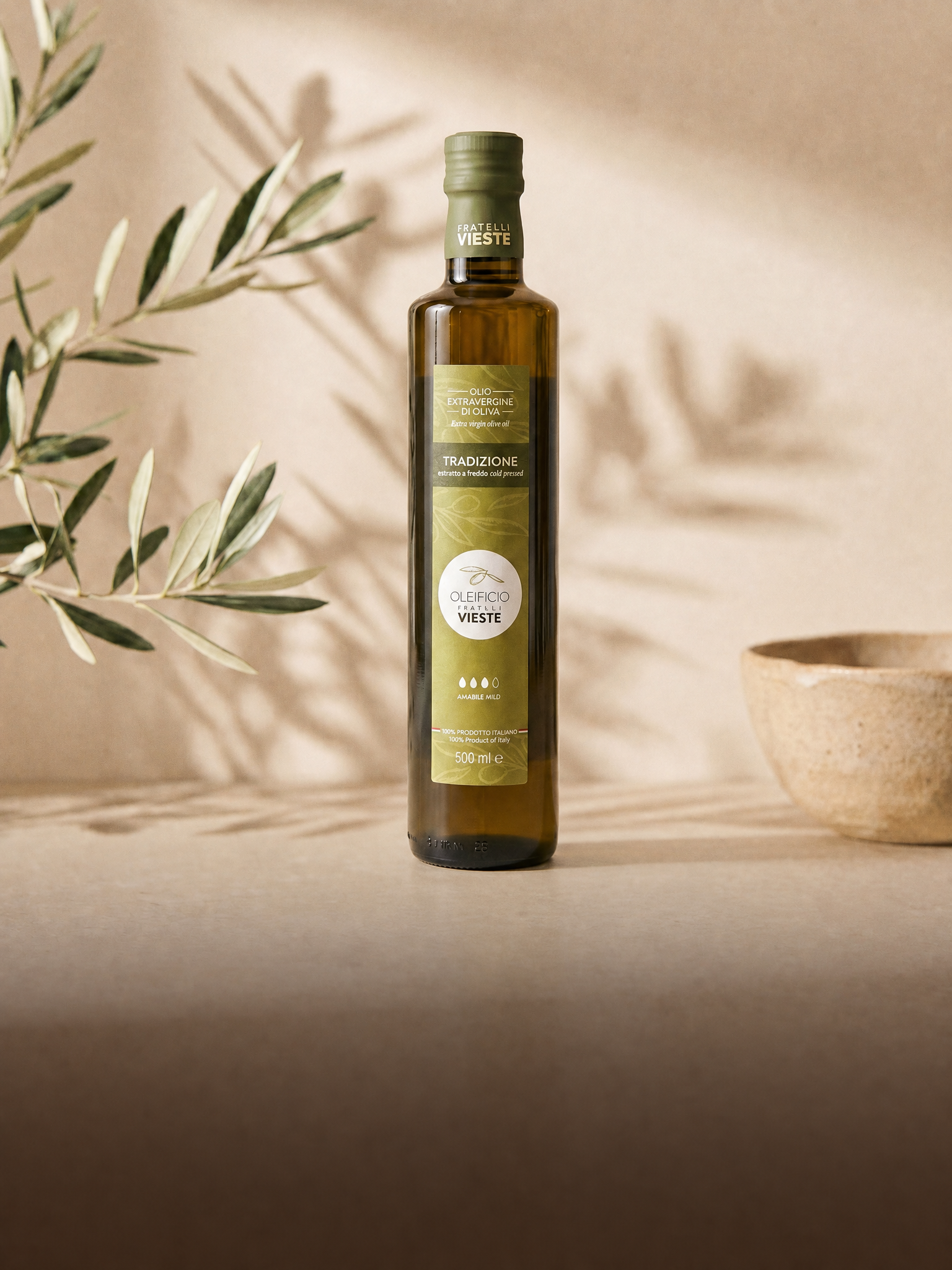 Bottiglia di olio extravergine Tradizione da 500 ml con rametto d'ulivo in luce calda. Oleificio Fratelli Vieste