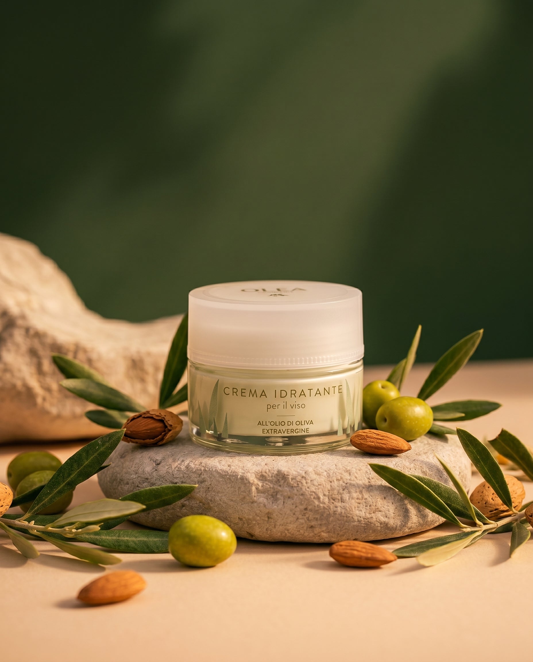 Il vasetto di crema idratante viso Olea su una pietra tra olive e mandorle. Oleificio Fratelli Vieste