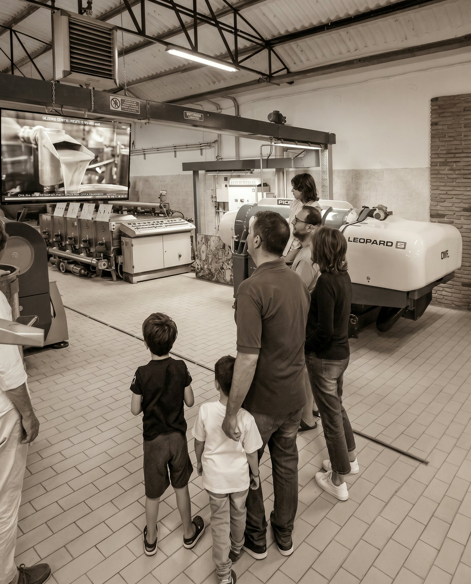 Adulti e bambini in visita al frantoio osservano le macchine della molitura. Oleificio Fratelli Vieste